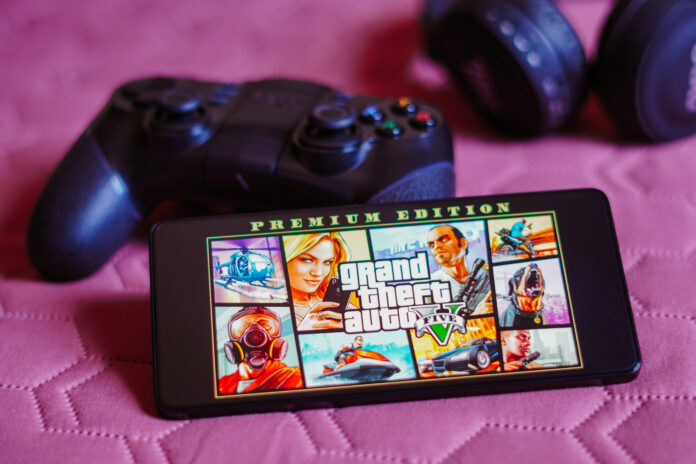 Grand Theft Auto V (GTA) logo is displayed on a smartphone screen, next to a gamepad